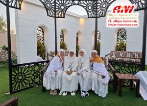 Five women in white traditional outfits pose on a bench inside a decorative black gazebo; Alhijaz Tour & Travel logo appears in the top-right corner.